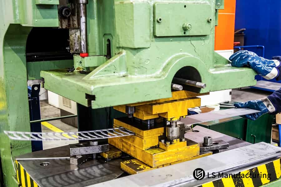 Workers load steel blanks into presses for automotive bracket production.